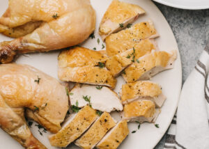 A carved roasted chicken on a white serving platter.