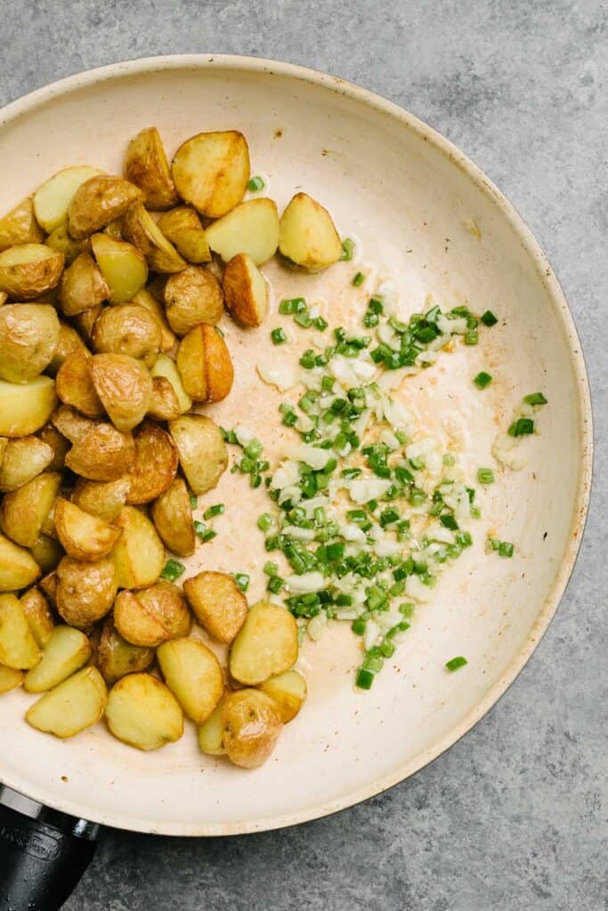 A skillet with crispy pan fried potatoes on one side and sautéed garlic and serrano chilies on the other side.