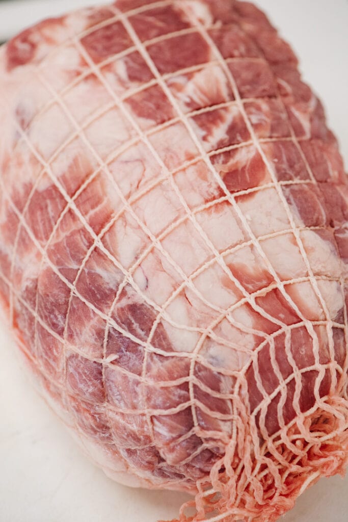 Side view, boneless pork butt on a cutting board wrapped in netting.