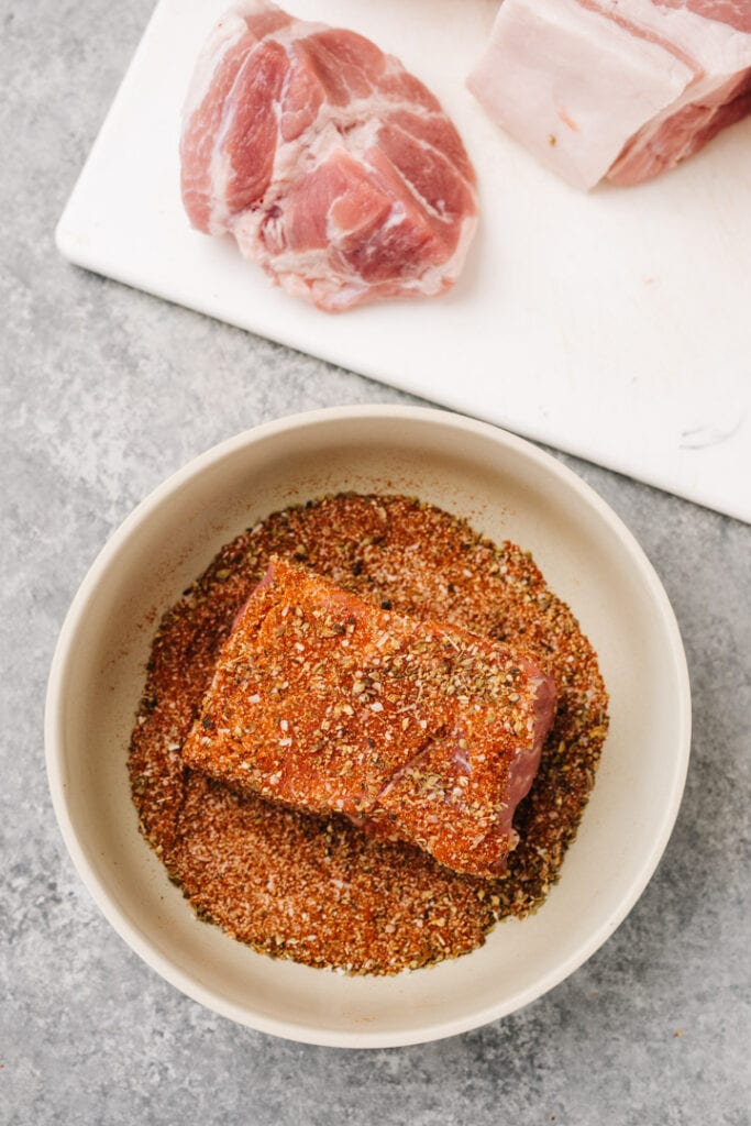 Coating a piece of pork in dry rub seasoning.