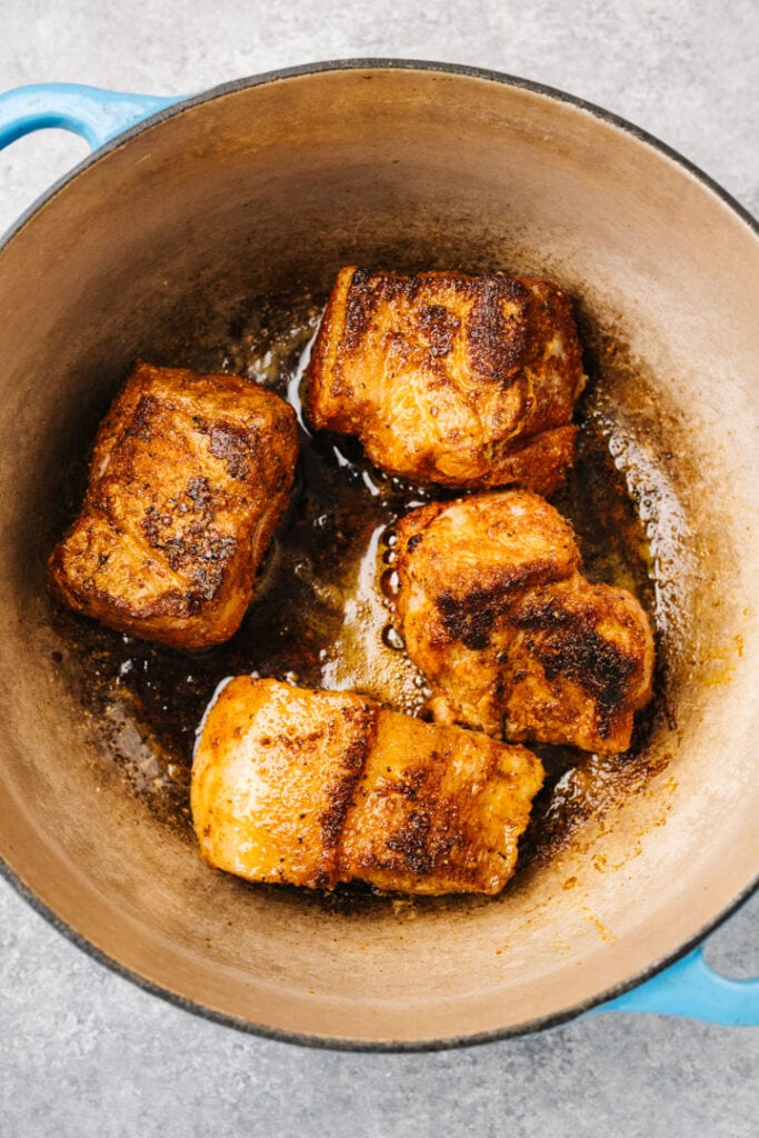 Pork pieces coated in dry rub searing in a dutch oven.