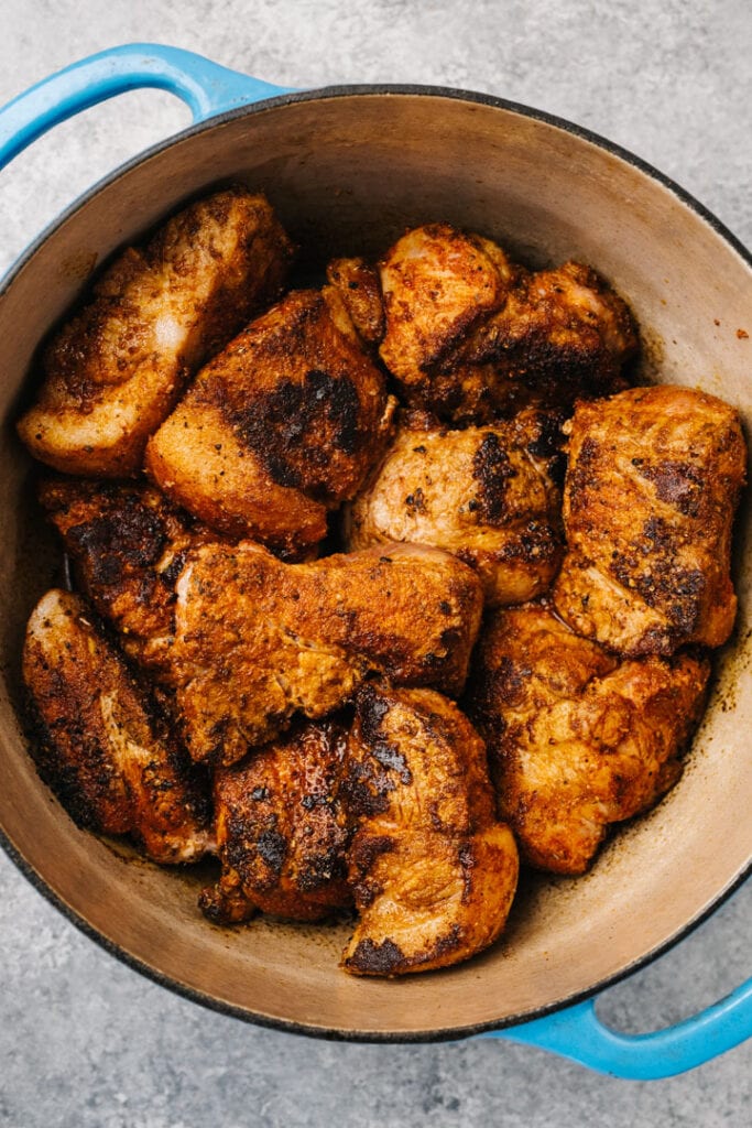 Seared pork pieces in a dutch oven before slow roasting in the oven.