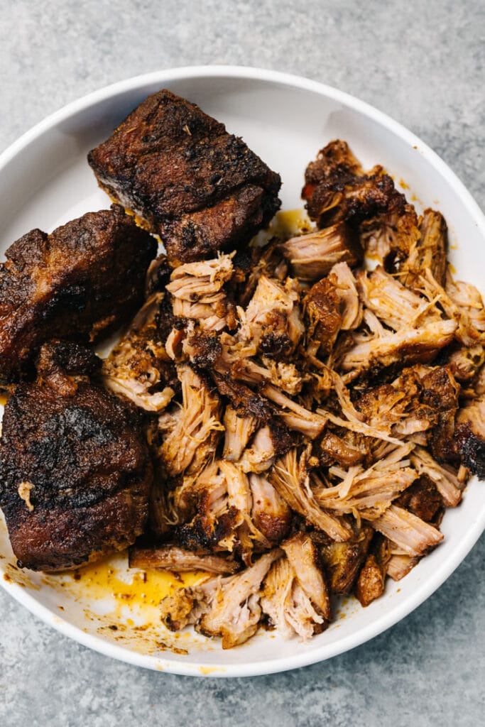 Partially shredded chunks of pulled pork in a white serving dish.