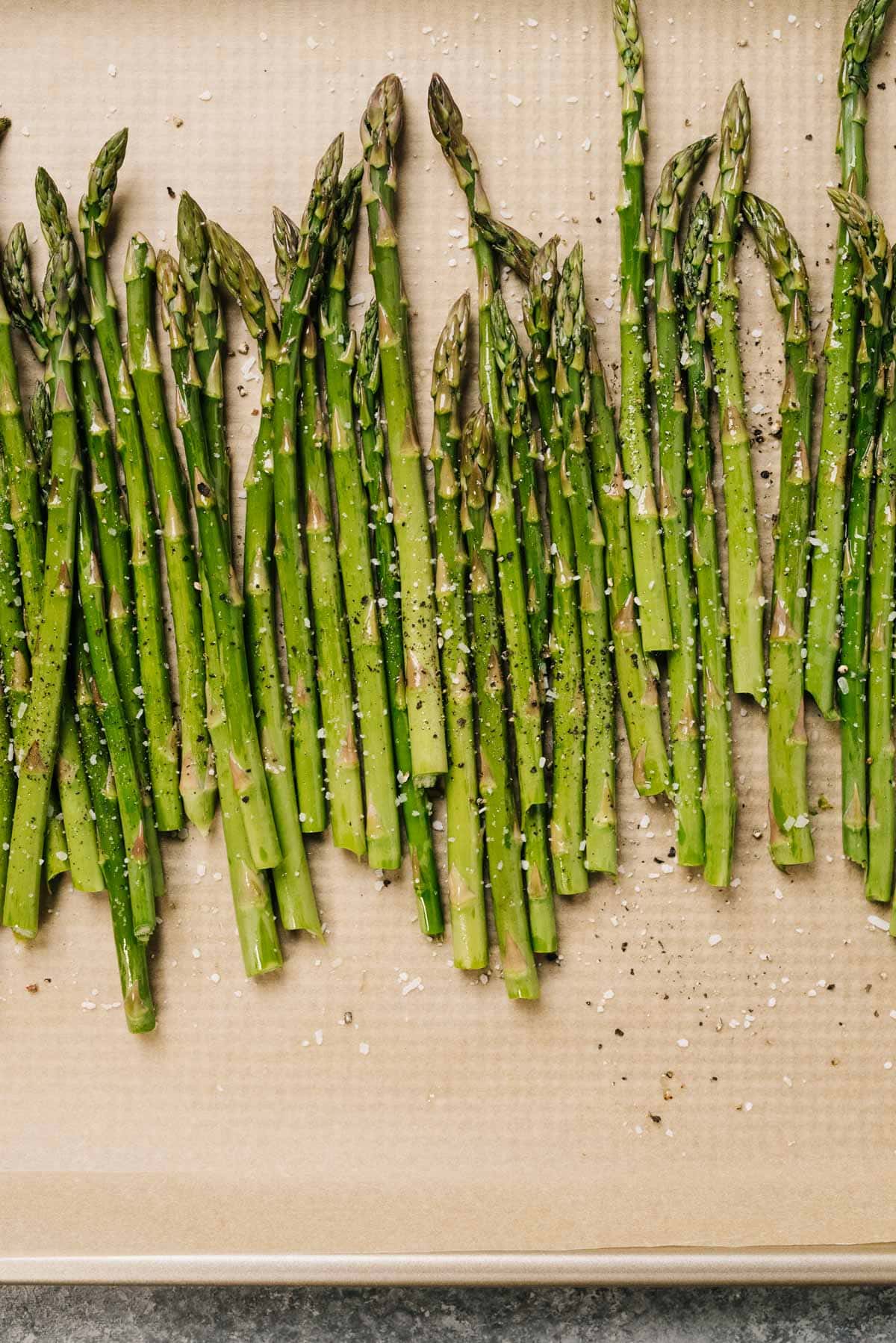 Asparagus spears tossed with olive oil, salt, and pepper on a parchment lined baking sheet.