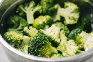 Side view, broccoli florets tossed with olive oil and salt in a metal mixing bowl.