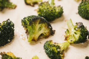 Side view, roasted broccoli florets in a single layer on a parchment lined baking sheet.