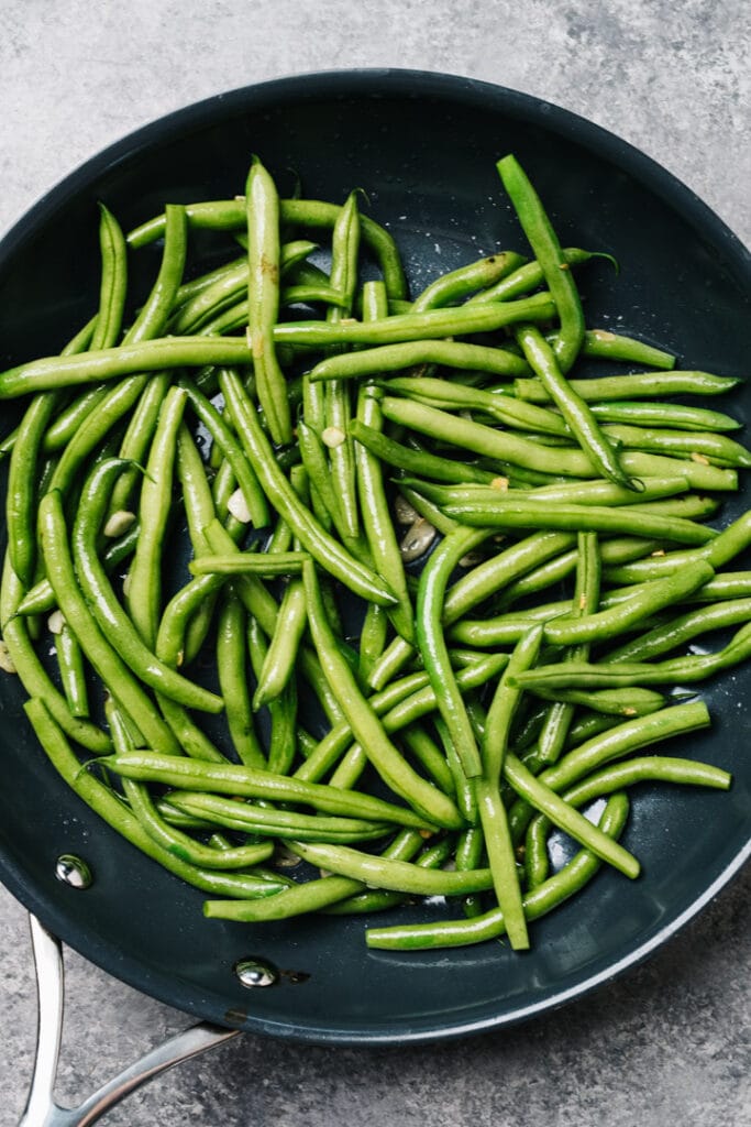 Green beans in a skillet with thinly sliced garlic.