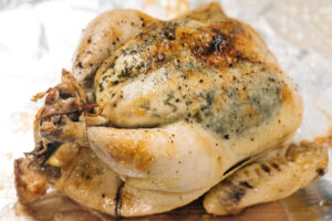 A whole slow cooker chicken on a foil lined baking sheet after crisping skin under the broiler in the oven.