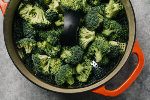 Broccoli florets in a steamed basket positioned in a dutch oven.