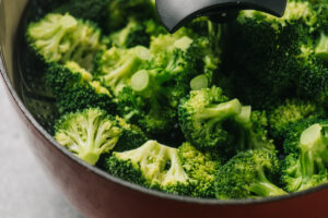 Side view, steamed broccoli florets in a steamed basket positioned in a dutch oven.