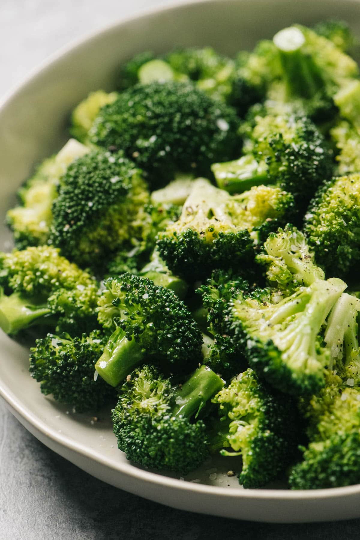 Side view, steamed broccoli in a tan serving bowl on a concrete background.