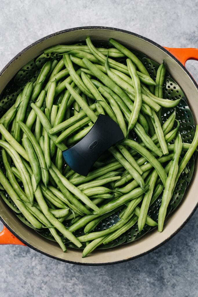 Green beans in a steamer basket fitted into a dutch oven.