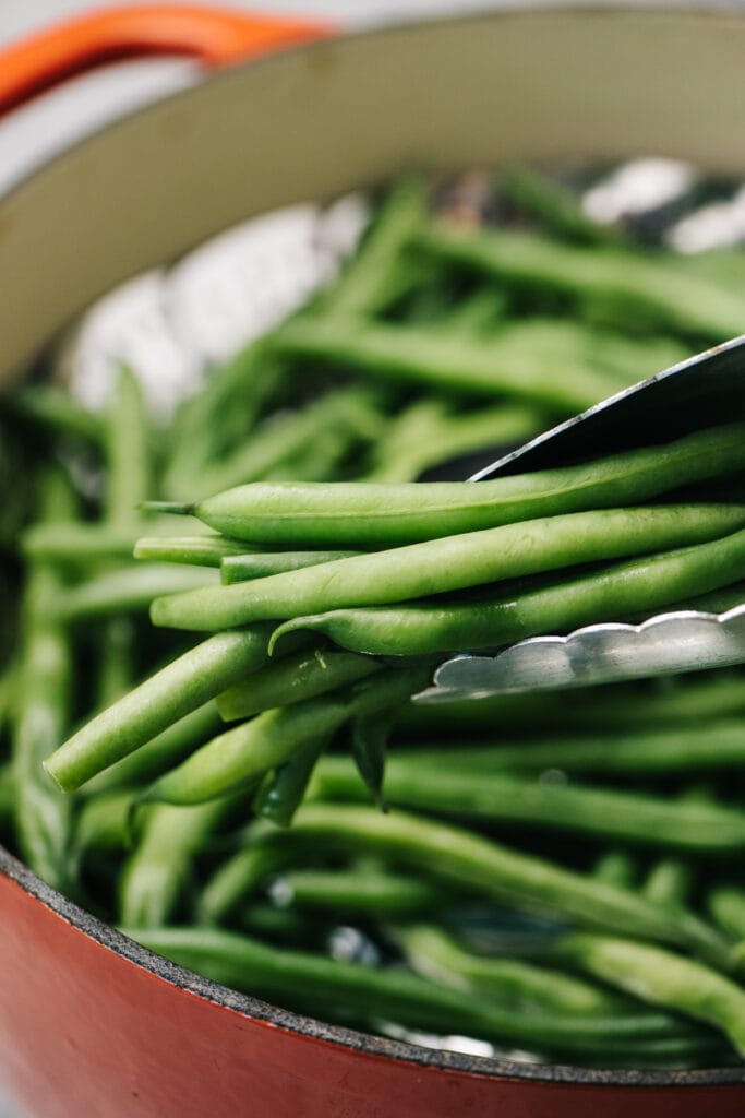 Tongs holding steamed green beans.