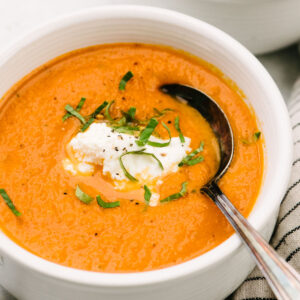 Side view, a spoon tucked into a bowl of fresh tomato basil soup garnished with ricotta cheese and basil.