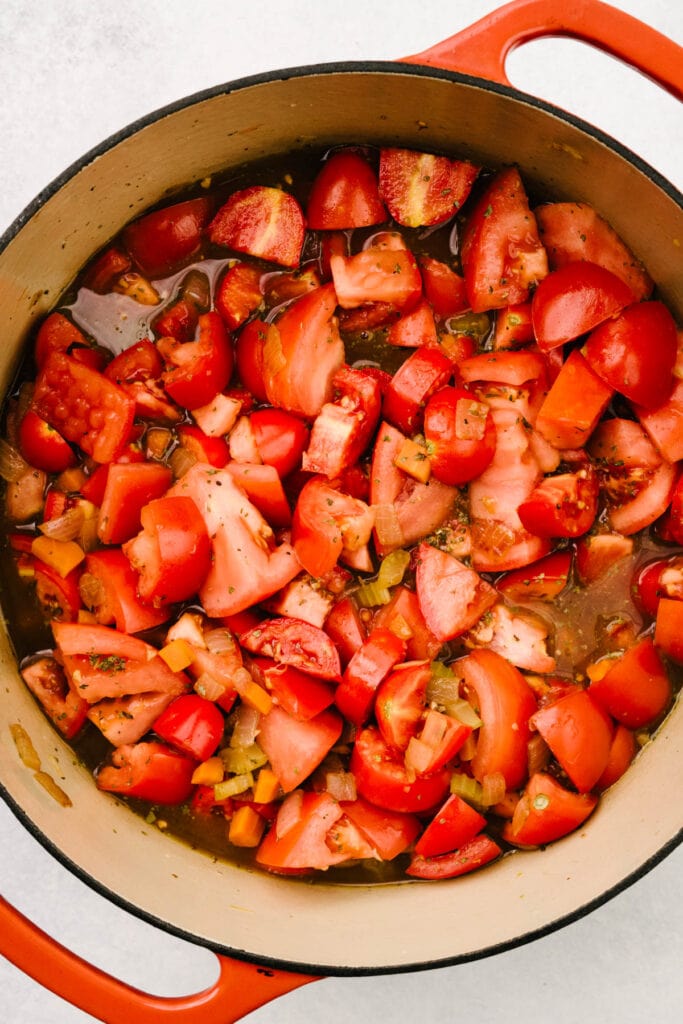 The ingredients for fresh tomato basil soup in a dutch oven - sauteed onions, carrots, celery, and garlic with dried basil and oregano, broth, and fresh chopped tomatoes.