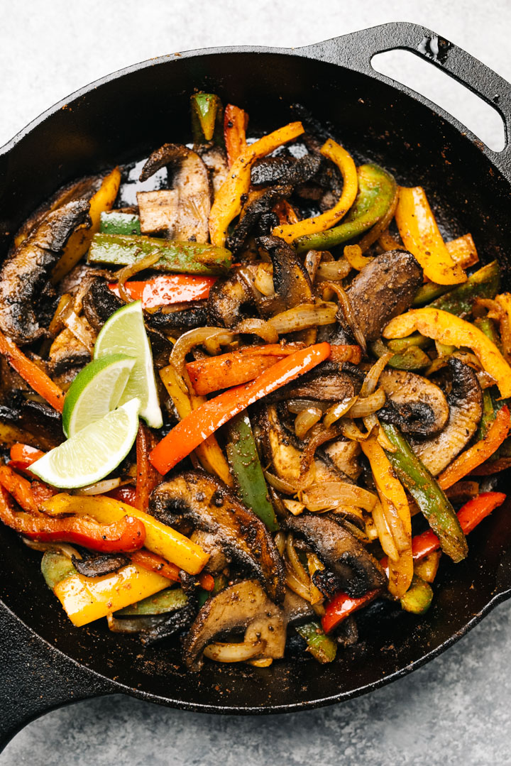 Portobello mushroom vegetarian fajita filling in a cast iron skillet, garnished with lime wedges.