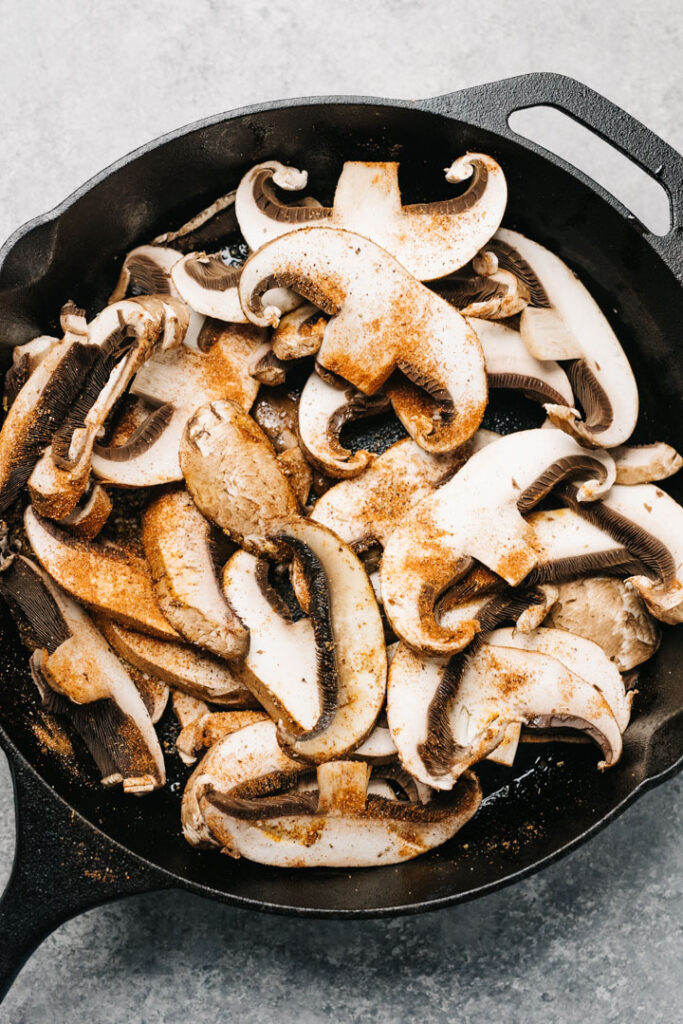 Sliced portobello mushrooms sprinkled with fajita seasoning in a cast iron skillet.