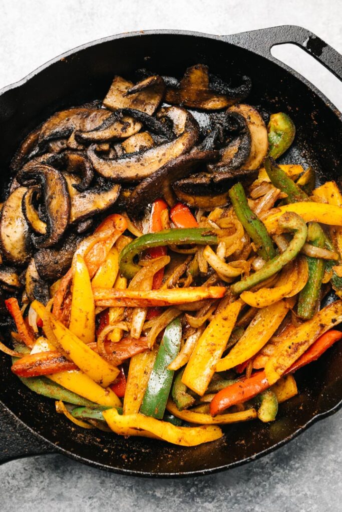 Sauteed vegetarian fajita filling in a cast iron skillet - portobello mushrooms, onions, and bell peppers.