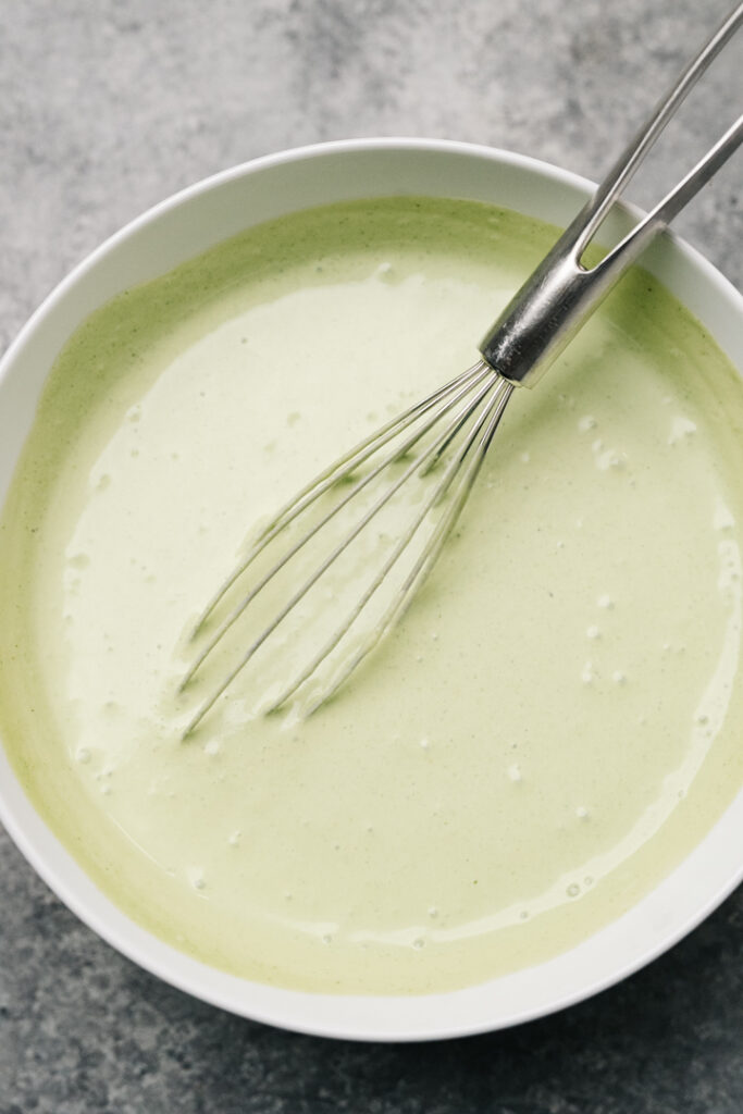 Cilantro lime sour cream in a small white bowl with a metal whisk.