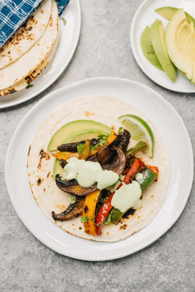 A tortilla on a white with vegetarian fajita filling, drizzled with cilantro lime sour cream.